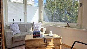 Um quarto aconchegante com um sofá, um conjunto de gavetas de madeira e uma janela com vista para árvores.