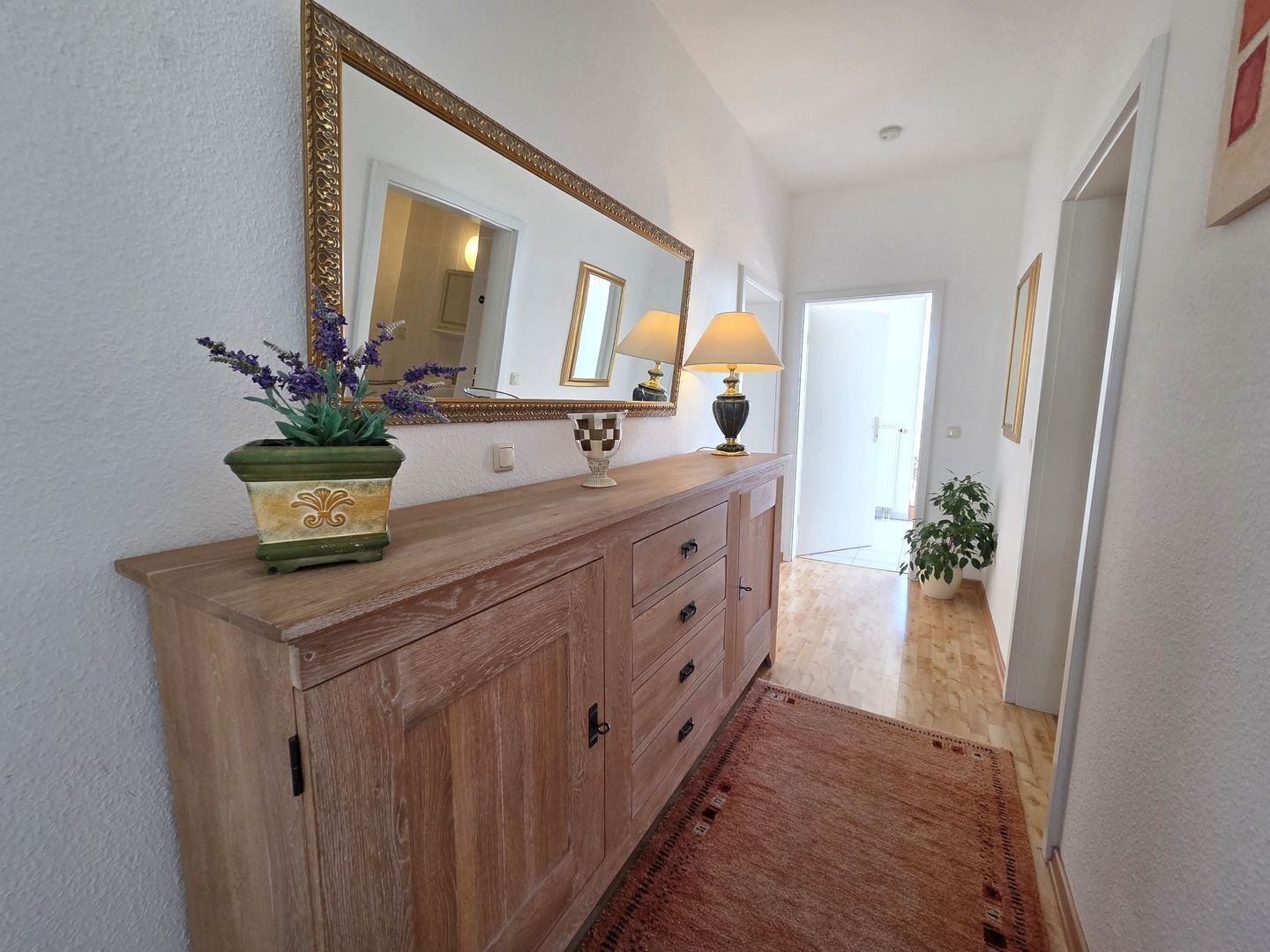 A hallway with a wooden console table, a large mirror, a lamp, and a potted plant.