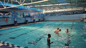 Una piscina interior con solárium de baldosas, techo alto con vigas metálicas y murales en las paredes.