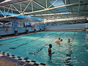 An indoor swimming pool with a tiled deck, a high ceiling with metal beams, and murals on the walls. - Sri Kavitha Nilayam (Hyderabad)