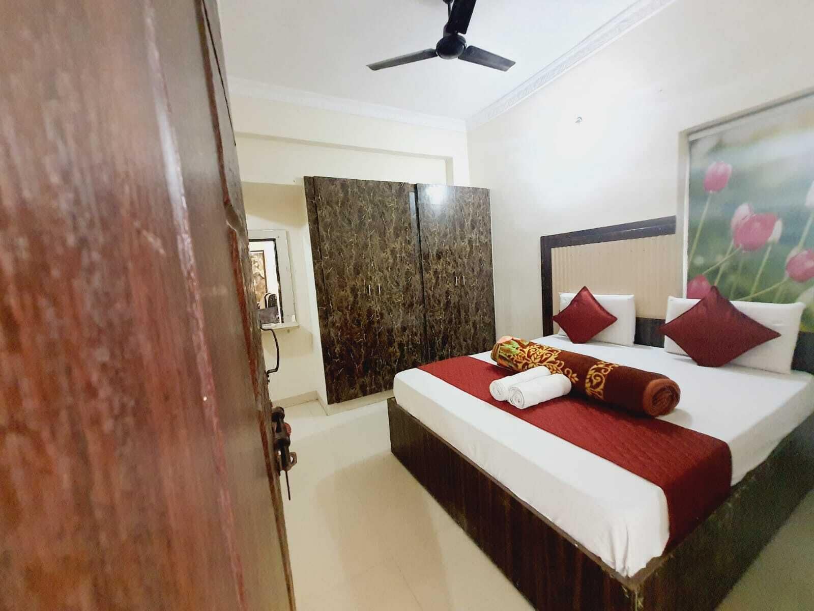Habitación de hotel con cama, ventilador de techo, armario y un cuadro de flores.