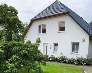 Ein zweistöckiges Haus mit weißer Fassade, dunklem Dach und einem kleinen Rosengarten.