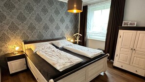 A bedroom with a bed, bedside lamps, a wardrobe, and a window with curtains. - Vacation apartment Seestern - Holiday apartment Seestern in Sassnitz on Rügen with (Sassnitz auf Rügen)