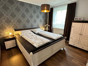 Ein Schlafzimmer mit Bett, Nachttischlampen, einem Kleiderschrank und einem Fenster mit Vorhängen.