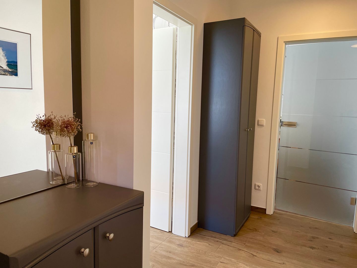 Une pièce avec un meuble sombre, une porte et un tableau encadré au mur.