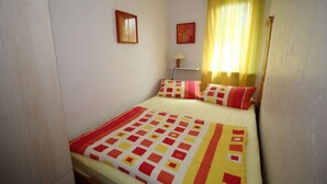 Un lit simple avec une couvre-lit à motifs, deux tableaux accrochés au mur et une fenêtre avec des rideaux jaunes.