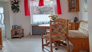 A room with a wooden dining table, a wooden chair, a sofa, a cabinet, and a window with red curtains. - Vacation home Figelski with terrace in Sassnitz - Holiday home Figelski in Sassnitz (Sassnitz auf Rügen)
