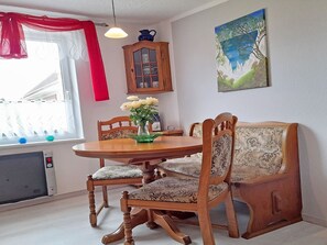 A dining area with a wooden table, four chairs, a vase with flowers, a cabinet, and a painting on the wall. - Vacation home Figelski with terrace in Sassnitz - Holiday home Figelski in Sassnitz (Sassnitz auf Rügen)