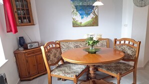 A dining area with a round wooden table, four chairs with floral upholstery, a painting on the wall, a clock, and a cabinet with glass doors. - Vacation home Figelski with terrace in Sassnitz - Holiday home Figelski in Sassnitz (Sassnitz auf Rügen)