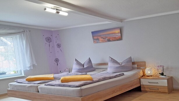 A modern bedroom with a wooden bed, a nightstand, a lamp, and a window with curtains. - Vacation home Figelski with terrace in Sassnitz - Holiday home Figelski in Sassnitz (Sassnitz auf Rügen)