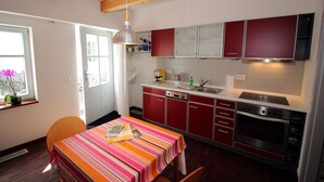 A kitchen with red cabinets, a stainless steel stove, and a window with a plant. - Vacation apartment Zum Strandvoigt (Sassnitz auf Rügen)