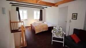 A room with a bed, a chair, a sofa, a desk, and a window. - Vacation apartment Zum Strandvoigt (Sassnitz auf Rügen)