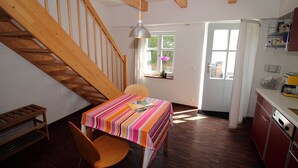 A dining area with a table, chairs, a wooden staircase, and a kitchen area. - Vacation apartment Zum Strandvoigt (Sassnitz auf Rügen)