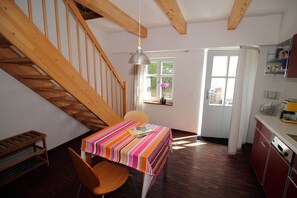 Ein Essbereich mit Tisch, Stühlen, einer Holztreppe und einer Küchenzeile.