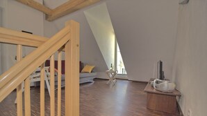 A loft-style room with a wooden staircase, a sofa, a small table with a speaker, and a large window. - Vacation apartment Zum Strandvoigt (Sassnitz auf Rügen)