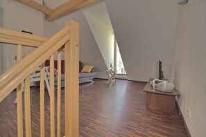 Ein Loft-Zimmer mit Holztreppe, einer Couch, einem kleinen Tisch mit Lautsprecher und einem großen Fenster.