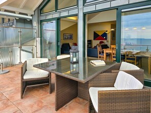 A glass-enclosed outdoor dining area with wicker furniture and a view of the interior. - Villa Friede-Marie, Penthouse Lenea - magnificent sea view over the Baltic Sea - (Sassnitz auf Rügen)