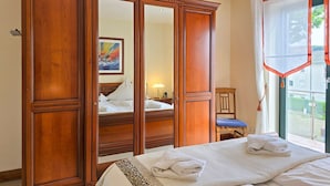 Quarto de hotel com um guarda-roupa de madeira grande, uma cama com roupa de cama branca, uma cadeira e uma janela com cortinas.
