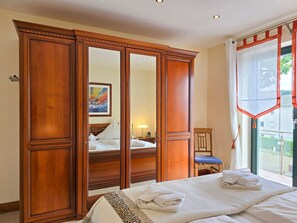 A hotel room with a large wooden wardrobe, a bed with white linens, a chair, and a window with curtains. - Villa Friede-Marie, Penthouse Lenea - magnificent sea view over the Baltic Sea - (Sassnitz auf Rügen)