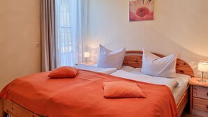 A double bed with an orange bedspread, two pillows, a wooden headboard, a nightstand with a lamp, and a wall-mounted picture. - Ferienhaus Zum Kreideblick, FW Seepferdchen - Holiday home Zum Kreideblick, (Sassnitz auf Rügen)