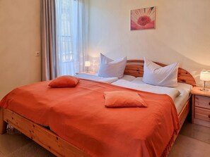 Ein Doppelbett mit orangefarbener Bettdecke, zwei Kissen, einem Holz-Kopfteil, einem Nachttisch mit Lampe und einem an der Wand hängenden Bild.
