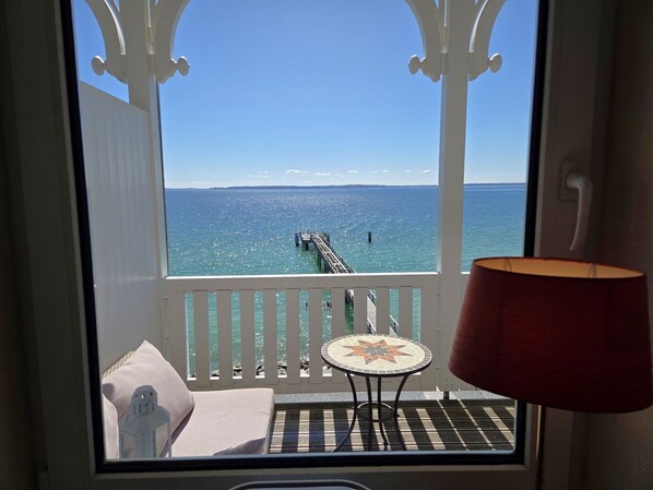 Ein Balkon mit Blick auf das Meer, eine Mole und ein kleiner Tisch mit einer Lampe.