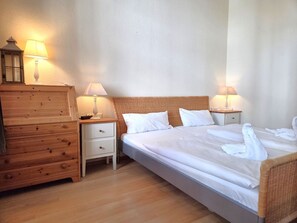 Ein Hotelzimmer mit einem hölzernen Schminktisch, einem Bett mit weißen Leinen, zwei Nachttischlampen und einem Rattan-Kopfstück.