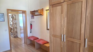 Un pasillo con armarios de madera, un banco con cojines rojos y un perchero de madera en la pared.