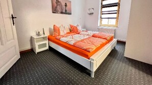 A bedroom with a bed, a nightstand, a window with blinds, and a painting on the wall. - Apartment 2 Otto - in the center of Sassnitz - Apartment 2 - only (Sassnitz auf Rügen)