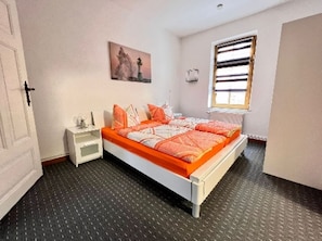 Ein Schlafzimmer mit Bett, Nachttisch, Fenster mit Jalousien und einem Bild an der Wand.