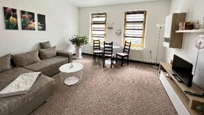 A living room with a sofa, a coffee table, two chairs, a TV on a stand, and a plant. - Apartment 2 Otto - in the center of Sassnitz - Apartment 2 - only (Sassnitz auf Rügen)