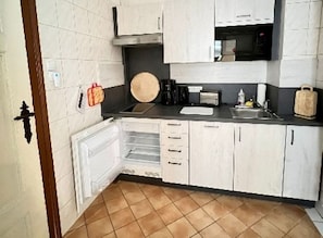 Eine kleine Küche mit weißen Schränken, einer Mikrowelle, einem Toaster und einem Spülbecken.