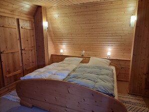 Ein Schlafzimmer mit Holzwänden, einem Bett, zwei Nachttischlampen und einer schrägen Decke.