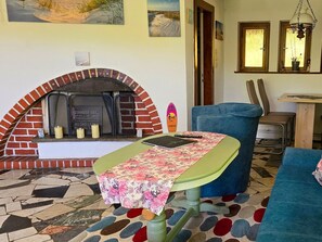Ein gemütliches Wohnzimmer mit Kamin aus Backstein, einem grünen Tisch mit Blumenmuster und einem blauen Sofa.