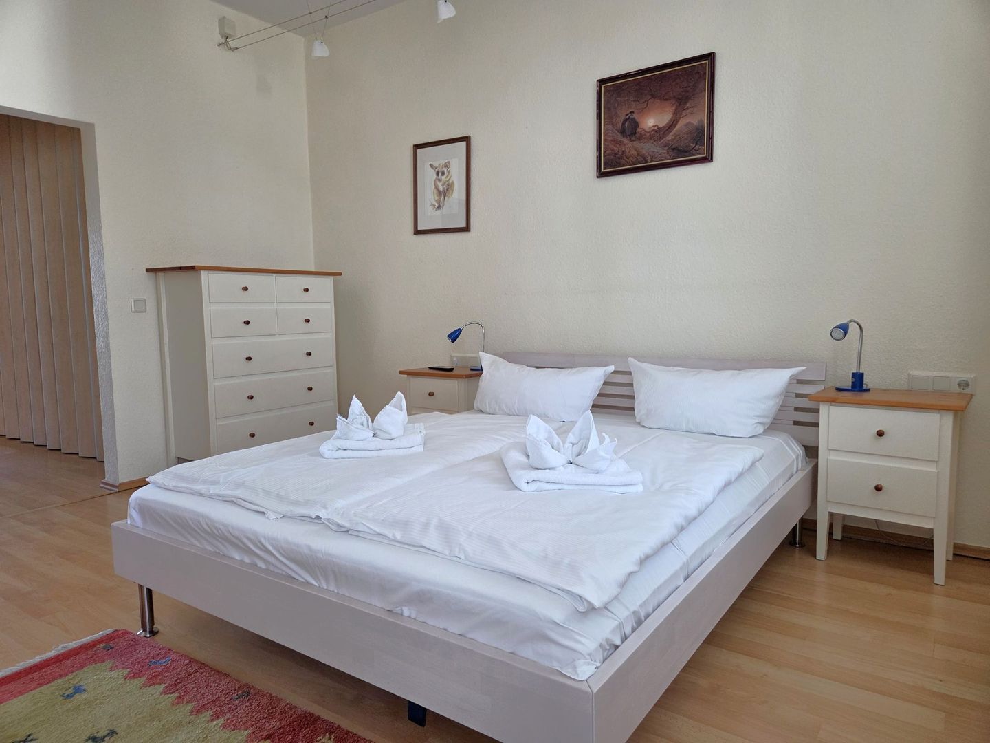 A hotel room with a large bed, two bedside tables, a wardrobe, and a painting on the wall.