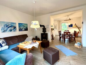 Ein Wohnzimmer mit einer Couch, einem Holztisch, einem Kamin, einer Essecke mit Stühlen und Kunstwerken an den Wänden.