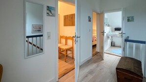 Un corridoio con pavimento in legno, uno specchio, una panca di legno e una porta che dà su una stanza con un letto e una finestra.