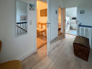 Ein Korridor mit Holzboden, einem Spiegel, einer Holzbank und einer Tür zu einem Zimmer mit Bett und Fenster.