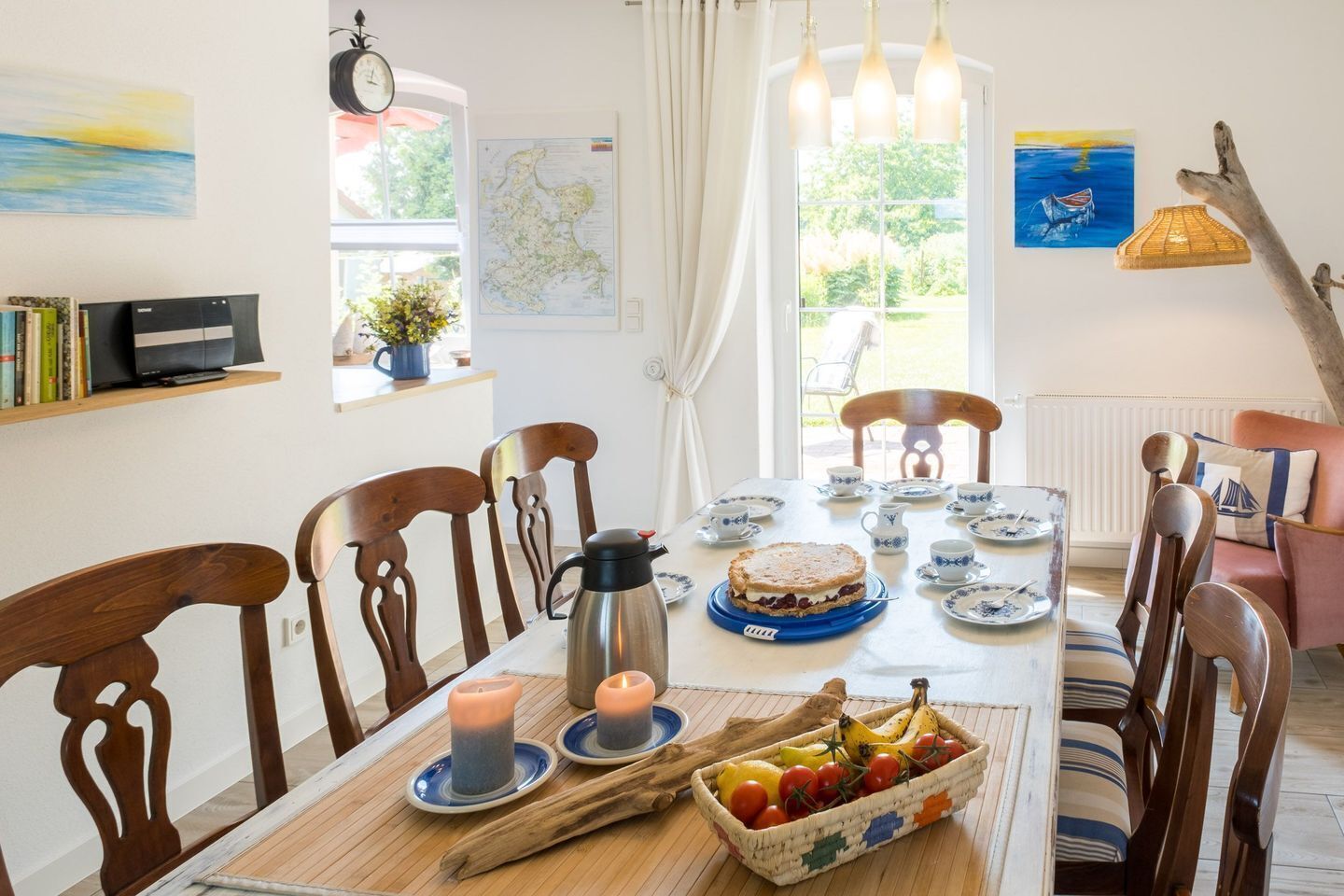 A dining room with a wooden table, chairs, a cake, fruit, and tea sets.