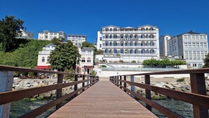 Un muelle de madera que conduce a una zona ribereña con edificios, incluyendo un hotel llamado 'FURSTENHOF' y 'STRANDHOTEL'.