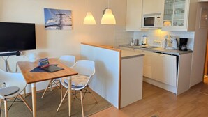 Habitación de hotel compacta con kitchenette, comedor con mesa y sillas, televisor y un cuadro en la pared.