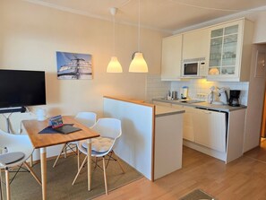 Ein kleines Hotelzimmer mit Küchenzeile, einem Essbereich mit Tisch und Stühlen, einem Fernseher und einem Bild an der Wand.