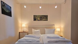Una cama doble con ropa blanca, dos mesitas de noche con lámparas, un cabecero y un cuadro en la pared.