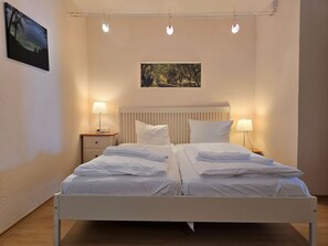 Ein Doppelbett mit weißen Bettwäsche, zwei Nachttische mit Lampen, ein Kopfteil und ein Bild an der Wand.