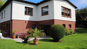 A two-story house with a brick base and white upper walls, a front door, and a small front yard with potted plants and a neatly trimmed bush. - Vacation apartment near the Bodden - Holiday apartment near the Bodden - idyllic on the large (Glowe OT Polchow)