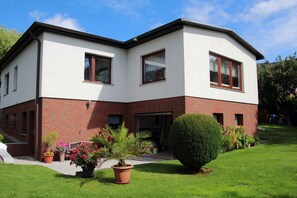 A two-story house with a brick base and white upper walls, a front door, and a small front yard with potted plants and a neatly trimmed bush. - Vacation apartment near the Bodden - Holiday apartment near the Bodden - idyllic on the large (Glowe OT Polchow)