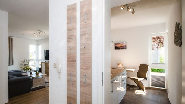 Een moderne woonkamer met een bank, salontafel en televisie. Er is een keuken met een eettafel en stoelen. De kamer heeft houten vloeren en witte wanden.