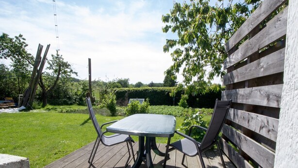 A wooden deck with a table and chairs, surrounded by a garden and a wooden fence. - Ferienzimmer am Försterberg - Holiday room Am Försterberg, on the edge of the (Lohme OT Hagen)