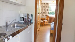 A kitchen with a sink, coffee maker, and cabinets. There is a dining area with a table and chairs. - Ferienzimmer am Försterberg - Holiday room Am Försterberg, on the edge of the (Lohme OT Hagen)