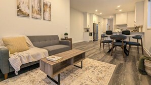 A modern living room with a sofa, coffee table, and dining area with chairs. - Quiet 2BR Condo Near Hospital and Wi-Fi (Mount Forest)
